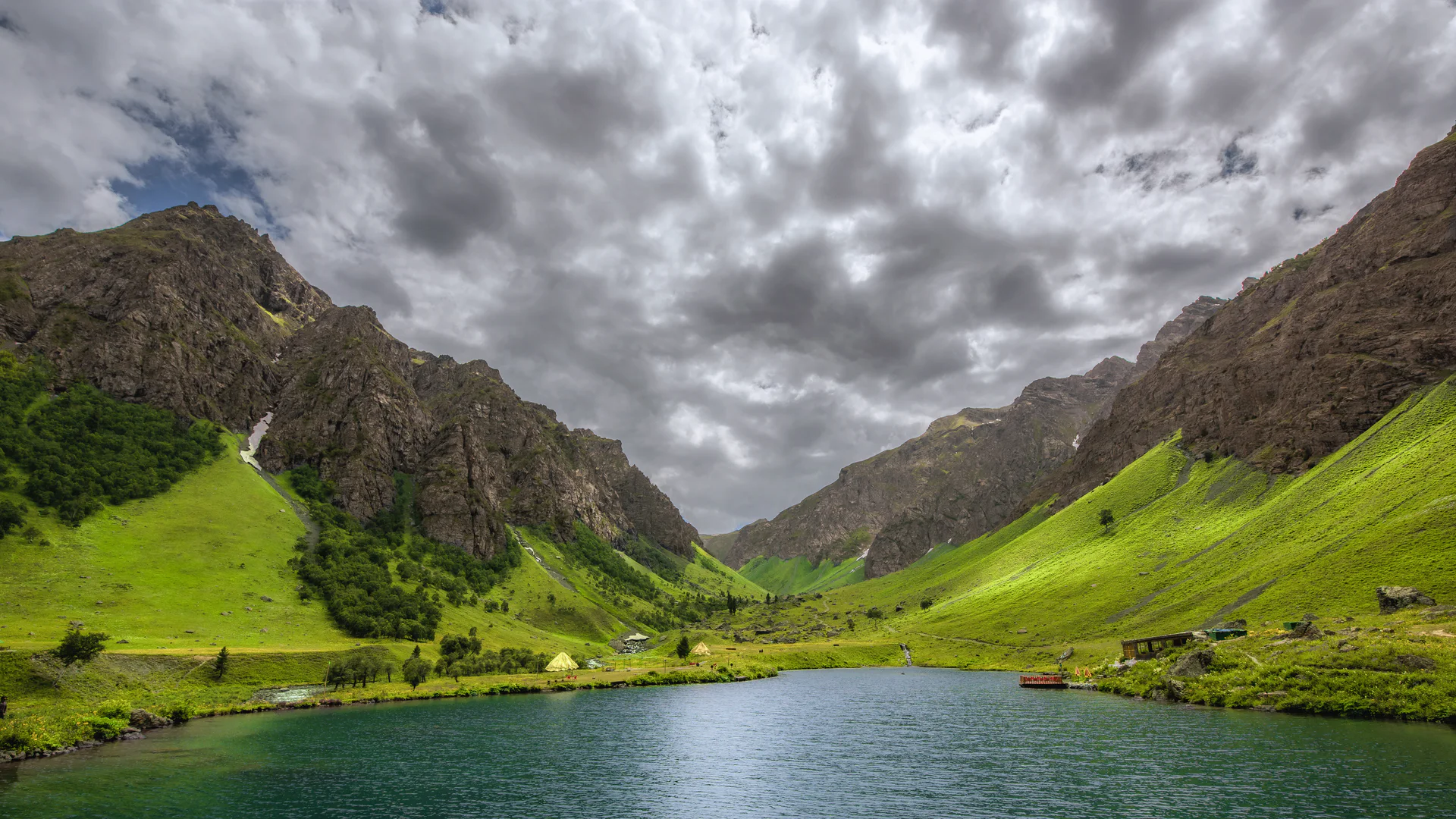 Clear Rainbow Lake between green meadows and high mountain slopes near Domel, Astore