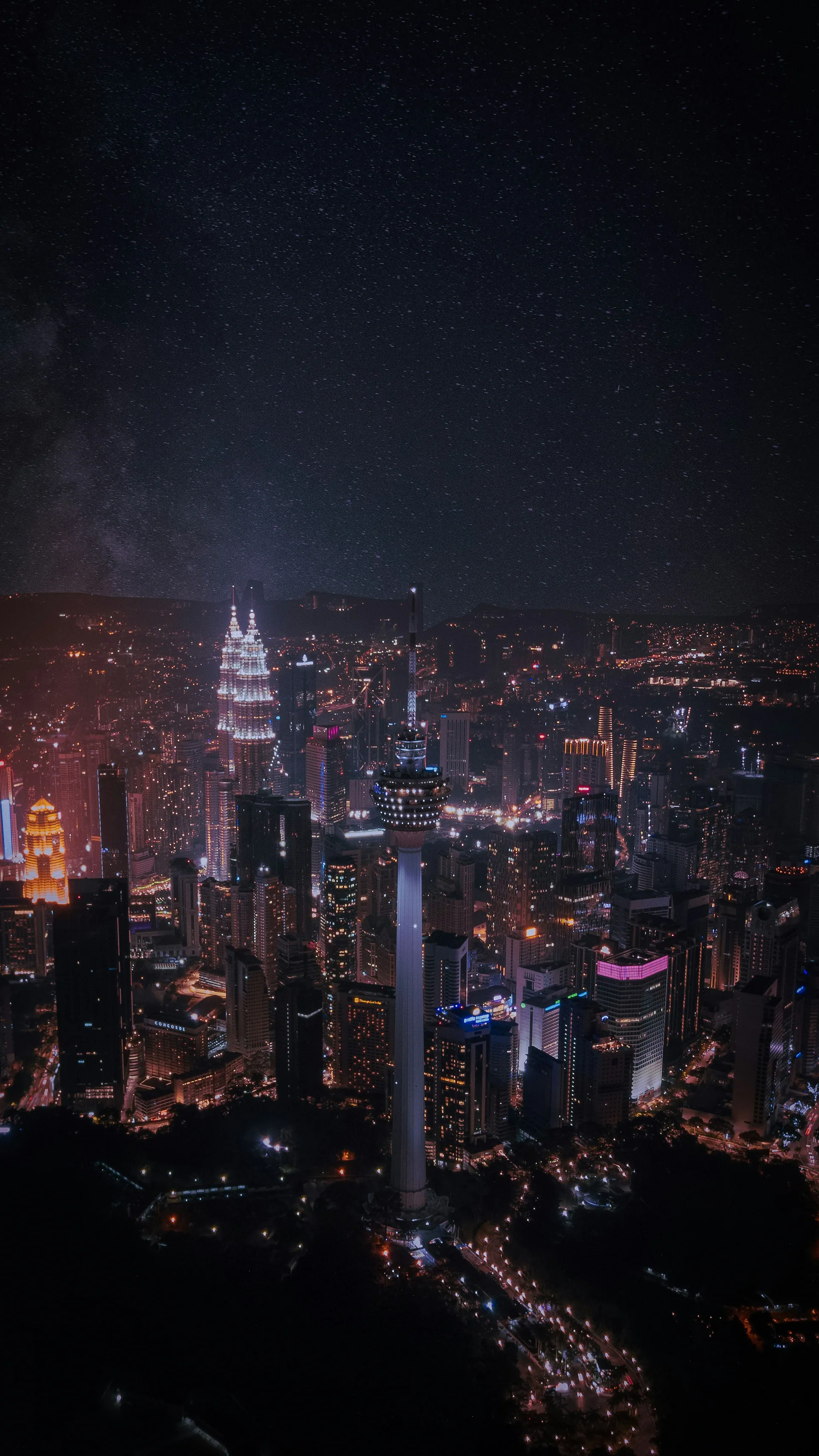 Kuala Lumpur Tower and the Petronas Twin Towers illuminated above the city at night