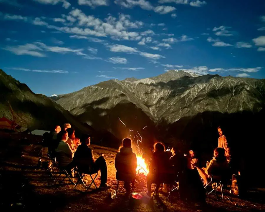 A group gathered around a nighttime campfire beneath mountains near Rakaposhi, Pakistan